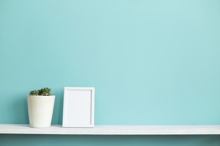 Modern room decoration with Picture frame mockup. White shelf against pastel turquoise wall with potted succulent plant.の写真素材
