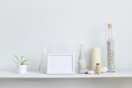 Modern room decoration with picture frame mockup. Shelf against white wall with decorative candle, glass and rocks. Potted spider plant.の写真素材