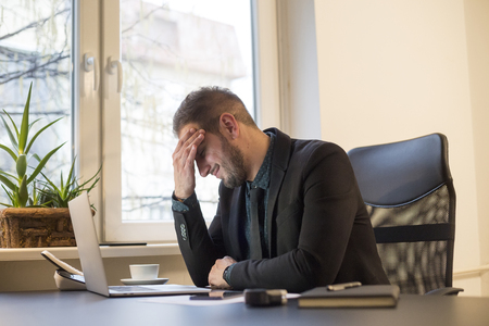 businessman working on laptop in office headache by window black table with notebook papers phone migraineの写真素材