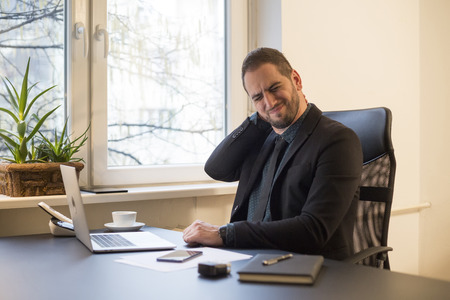 businessman working on laptop in office neck hurt by window black table with notebook papers phoneの写真素材