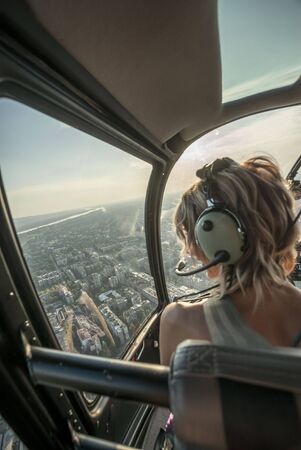 Portrait of beautiful blonde women enjoying helicopter flight. She is amazed by cityscape and wearing pilot headphones.の写真素材