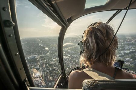 Portrait of beautiful blonde women enjoying helicopter flight. She is amazed by cityscape and wearing pilot headphones.の写真素材