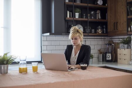 Focused young woman working on small business start up with a laptop. She is sitting at her kitchen table at home.の写真素材