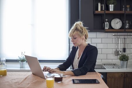 Focused young woman working on small business start up with a laptop. She is sitting at her kitchen table at home.の写真素材