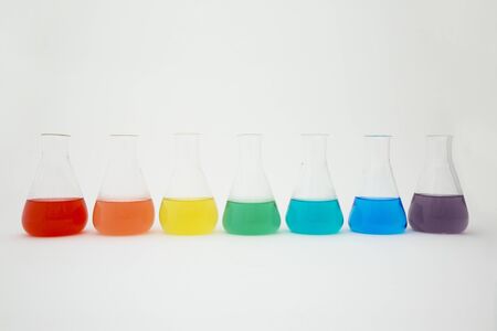Scientific laboratory glass erlenmeyer flask filled with colorful liquid forming rainbow on white background.の写真素材