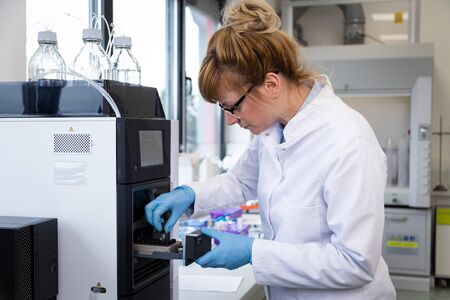 Female chemical scientist wearing glasses and rubber gloves takes samples of CBDa oil from small slot in chromatography machine during pharmaceutical laboratory experiment. Healthcare pharmacy from cannabis.の写真素材