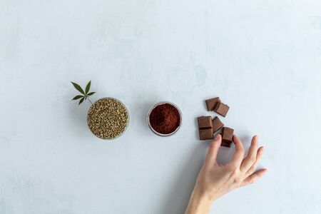CBD cannabis chocolate, cocoa and hemp seed on bright background. Hand taking chocolate. Medicinal marijuana in food.の写真素材