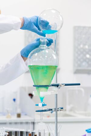 Close up shot of hand wearing rubber gloves work with blue liquid in separatory funnel that is place. Laboratory environment.の写真素材