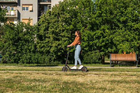 Young beautiful girl rides an electric scooter through an urban settlement with older buildings in the background.の写真素材