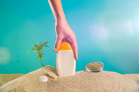 Sunscreen from CBD products and twigs of the marijuana plant in the sand. Around the product you can...