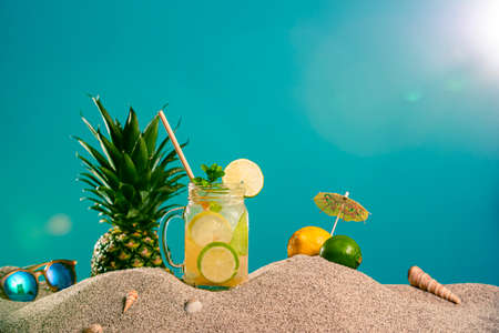 Lemonade in different glasses / jars, CBD dropper oil and a twig of marijuana plant in the sand....