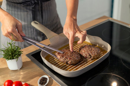 A close-up view of baking a burger on a grill pan in the kitchen, while the chef gently flips the burger and checks its readiness.の写真素材
