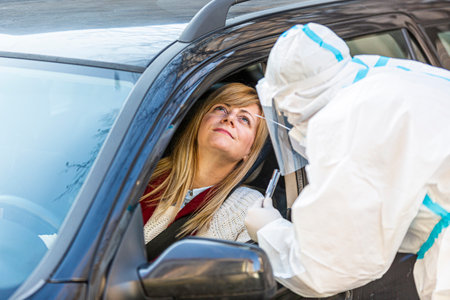 Woman sitting in car, waiting for medical worker to perform drive-thru COVID-19 test, taking nasal swab sample through car window, PCR diagnostic for Coronavirus, doctor in PPE holding test kit.の写真素材
