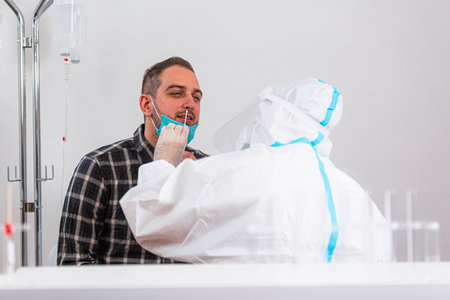 Medical worker performing COVID-19 test, taking nasal swab sample from male patient in hospital lab,...