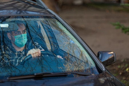 Man driving a car in a medical mask. Man in protective mask is sitting at the wheel of a car....