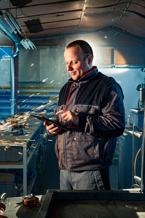 The handyman with a tablet in his workshop typing something, while in the background his colleague...