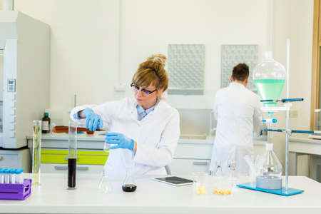 Female chemical scientist wearing glasses works with hemp CBD and CBDa oils in laboratory. She uses...