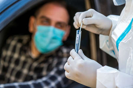 Man sitting in car, waiting for medical worker to perform drive-thru COVID-19 test, taking nasal swab sample through car window, PCR diagnostic for Coronavirus, doctor in PPE holding test kit.の写真素材