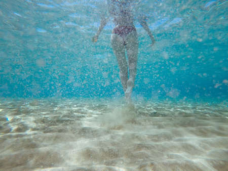 Rear underwater view of woman in bikini walking on sand under the sea.の写真素材