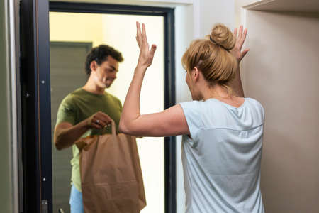 A food delivery man in front of the open door of the apartment, in a situation where he justifies himself to a woman who received package that was late.の写真素材