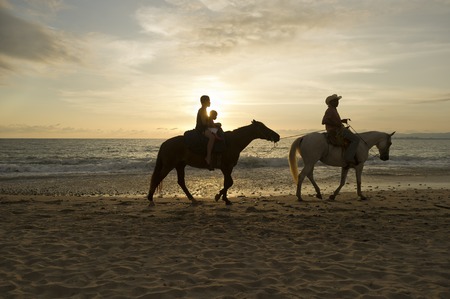 A woman and he child are led by a man on a beach horseback rideの写真素材