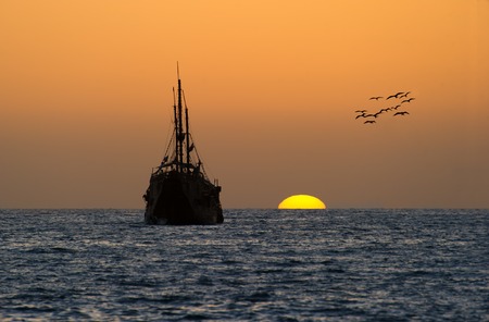 An old wooden pirate ship sits on the water with the colorful cloudscape sunset above.の写真素材