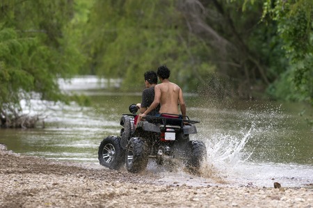Quad bike ATV is a couple of young riders having an exciting ride while splashing water and dirt at the edge of the river.の写真素材