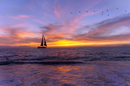 Sailboat sunset silhouette is a colorful vibrant orange and yellow cloudscape sunset.の写真素材