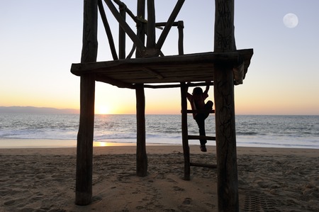 Boy Beach is a little boy at the beach silhouetted against a sunset sky while playing in his wooden fort.の写真素材