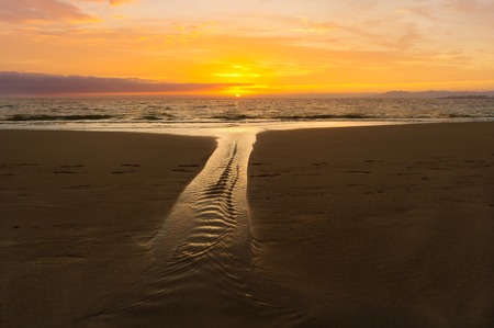 Ocean sunset is a sandy beach scenic with a soft flowing stream and a vivid vibrant sunset sky on the horizon.oceansunsetの写真素材