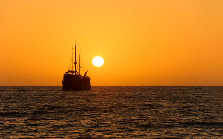 Ocean sunset ship silhouette is an old wooden ship sitting at sea watching the sunset on the ocean horizon.の写真素材