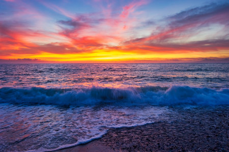 A Colorful Ocean Sunset Sky as a Gentle Wave Rolls to Shoreの写真素材