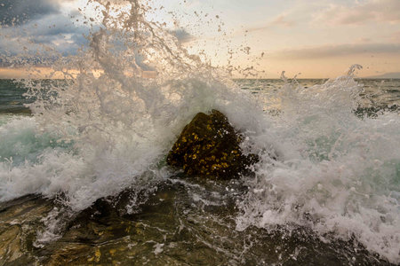 A Wave Is Breaking And Splashing On Sea Rocks As Ocean Spray Is Captured In Mid Air