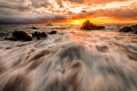 A Sailboat Is Sailing Along The Ocean With A Wave Breaking On Shore And Bird Flying Overhead