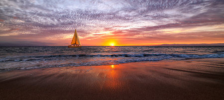 A Sailboat Is Sailing Along The Ocean With A Wave Breaking On Shoreの写真素材