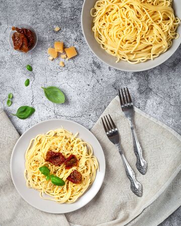 Two plates of prepared spaghetti with basil and dried tomatoesの写真素材