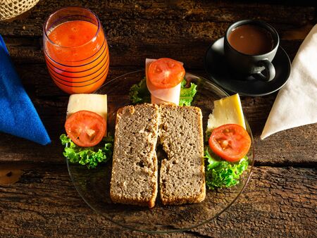 Homemade bread without gluten ready to prepare a sandwich with lechucha, cheese, ham and tomato. And, to drink, papaya juice and chocolate served in a black cup and wooden cutleryの写真素材