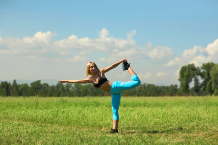 Beautiful sport woman doing stretching fitness exercise in city park at green grass. Yoga posturesの写真素材