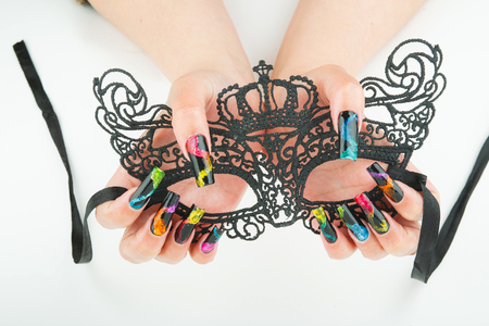 hands with beautiful manicure holding a black lace carnival mask on white backgroundの写真素材
