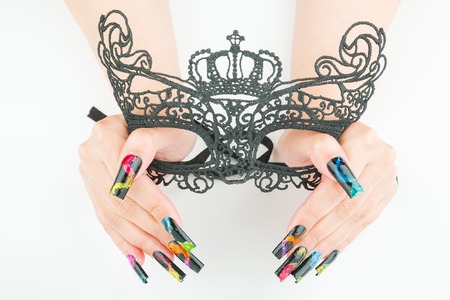 hands with beautiful manicure holding a black lace carnival mask on white backgroundの写真素材