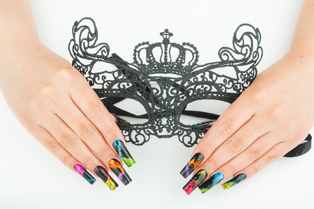 hands with beautiful manicure holding a black lace carnival mask on white backgroundの写真素材