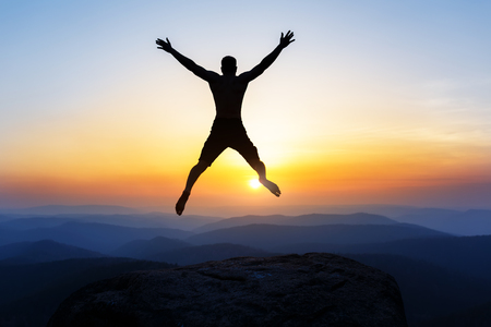 Happy man jumping for joy on the peak of the mountain, cliff at sunset. Success, winner, happinessの写真素材