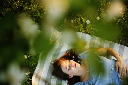 Beautiful woman enjoying daisy field, nice female lying down in the meadow of flowers, pretty girl relaxing outdoor, having fun, happy young lady and spring green nature, harmony and freedom conceptの写真素材