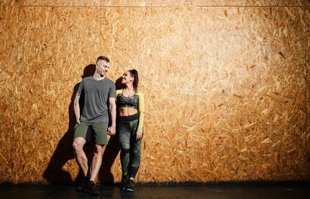 Portrait of a couple of young male and female athletes in sportswear standing near a wooden wall. The concept of a healthy lifestyle and daily workoutsの写真素材