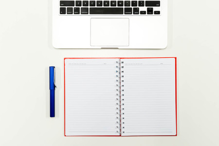 Flat lay photo of white office desk with laptop keyboard, pen and notebook, top viewの写真素材