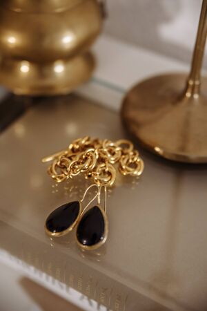 gold earrings with black gem and gold chain in the interiorの写真素材