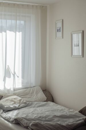 white room with white linens blanket and pillows white walls with paintings and sunbeams in cozy...