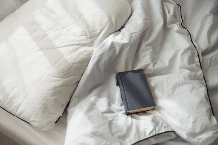 book gray on a white bedding quilt and sunbeamsの写真素材