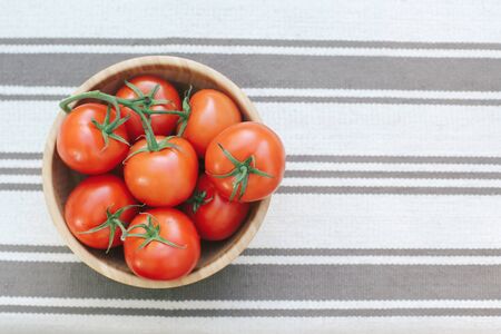 A lot of red tomatoes in a wooden plate, on a background of greens.の写真素材