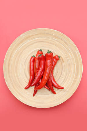 Many lined up, fresh chili peppers on a plain pink background.の写真素材